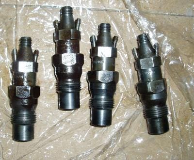 Four metal fuel injectors on a surface.