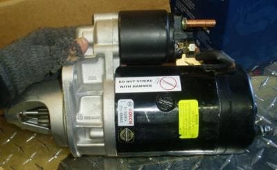 Black automotive starter motor with warning label.