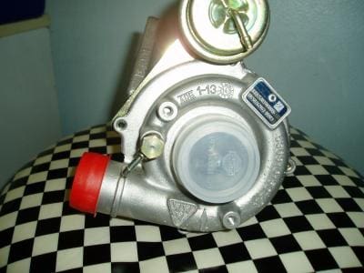 Silver turbocharger with red cap on checkered surface.